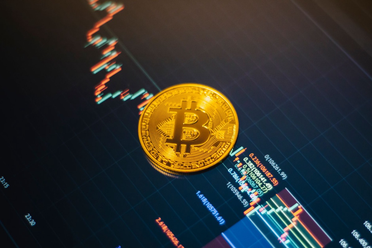 Bitcoin coin placed next to financial trading charts on a screen