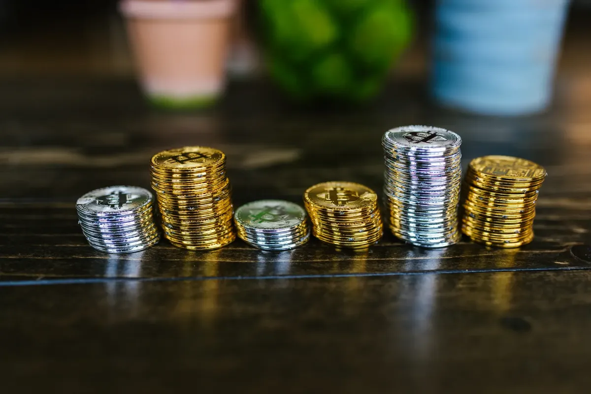 木桌上堆疊著閃亮的黃金與銀色加密貨幣硬幣。
